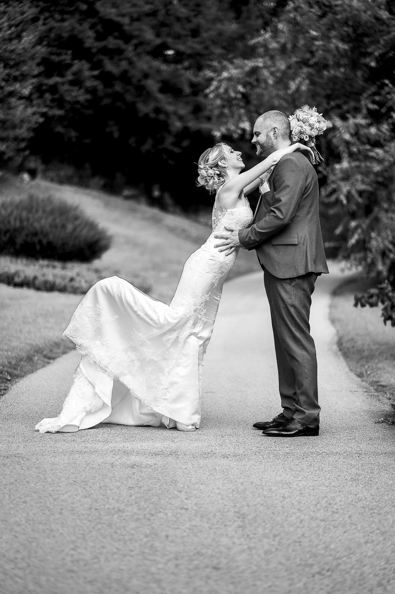 La mariée enlace son mari sur une allée bordée d'arbres La mariée enlace son mari sur une allée bordée d'arbres