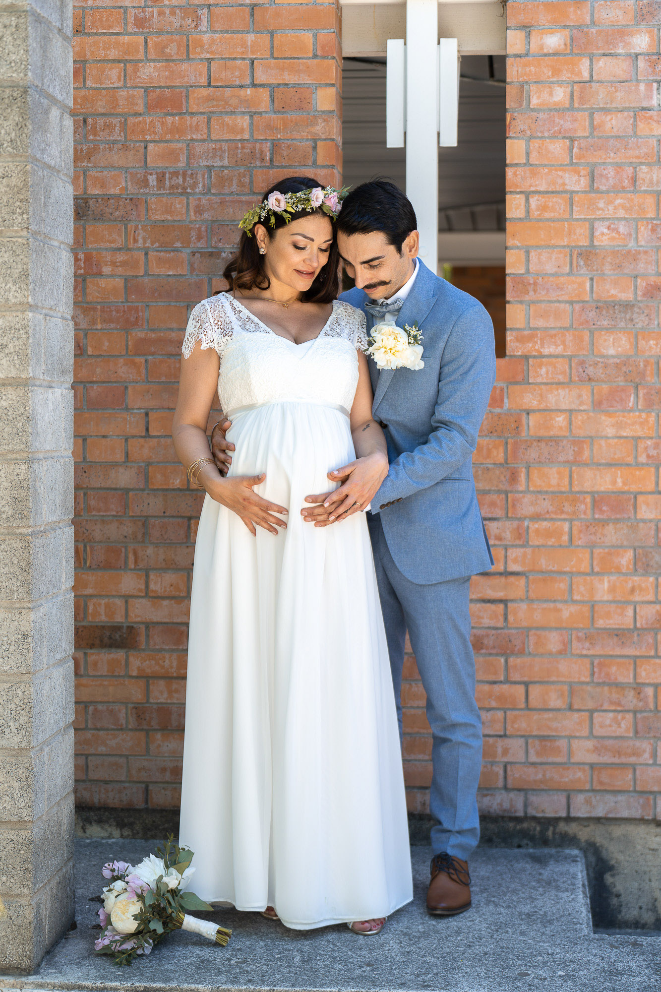 Mariée enceinte en robe de dentelle et couronne de fleurs, aux côtés de son mari Mariée enceinte en robe de dentelle et couronne de fleurs, aux côtés de son mari